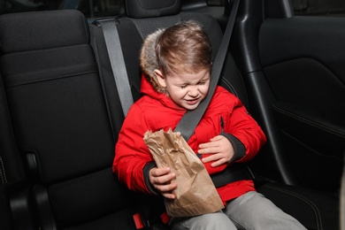 Little boy with paper bag suffering from nausea in car