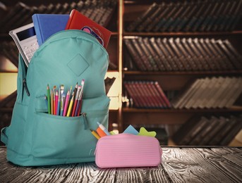 Backpack with school stationery on wooden table in library, space for text