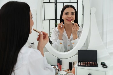 Beautiful woman applying makeup near mirror in room