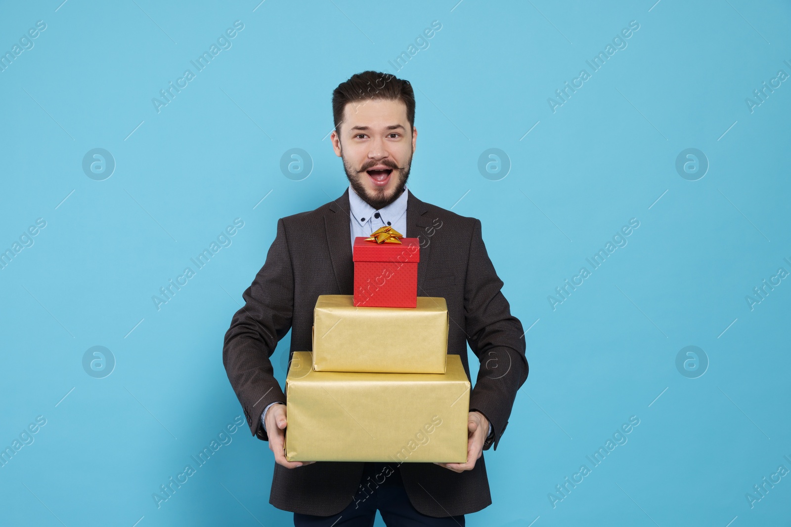 Photo of Emotional man in suit with stack of gifts on light blue background