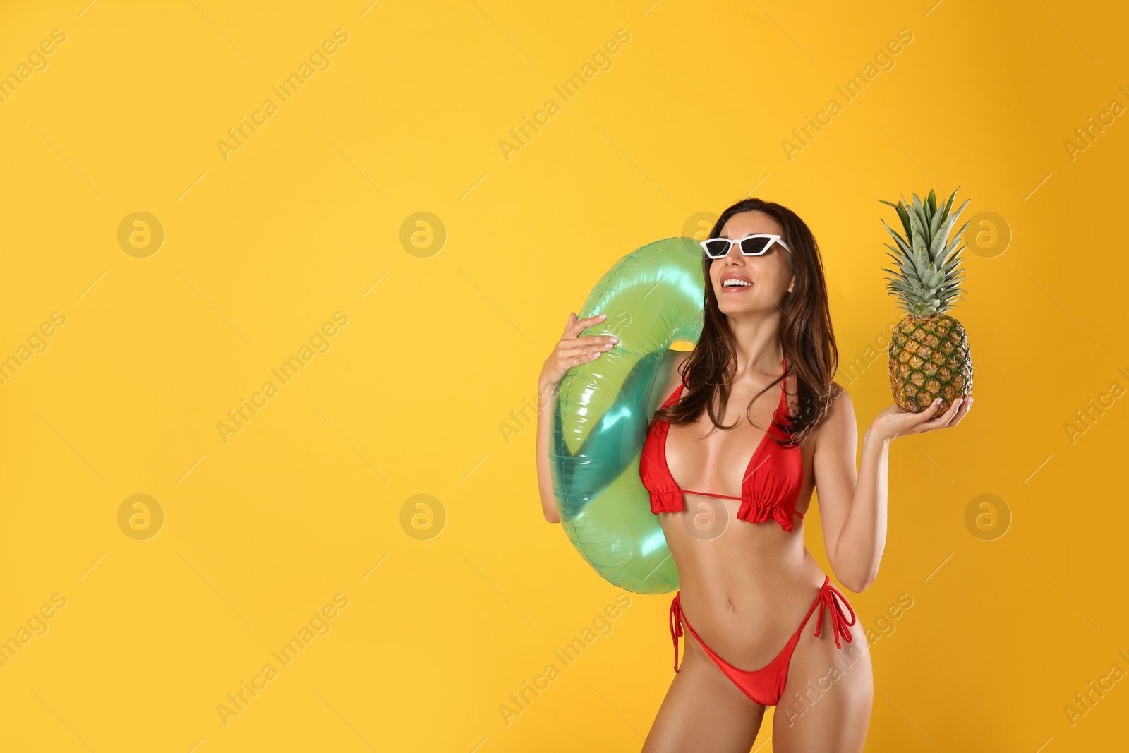 Photo of Beautiful woman in stylish bikini with pineapple and inflatable ring on yellow background. Space for text