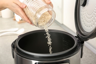 Photo of Woman pouring rice from jar into cooker in kitchen, closeup