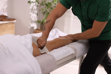 Woman receiving professional leg massage with gua sha on couch in spa salon, closeup