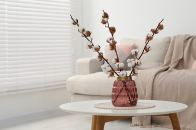 Photo of Cotton branches with fluffy flowers on white table in cozy room. Space for text