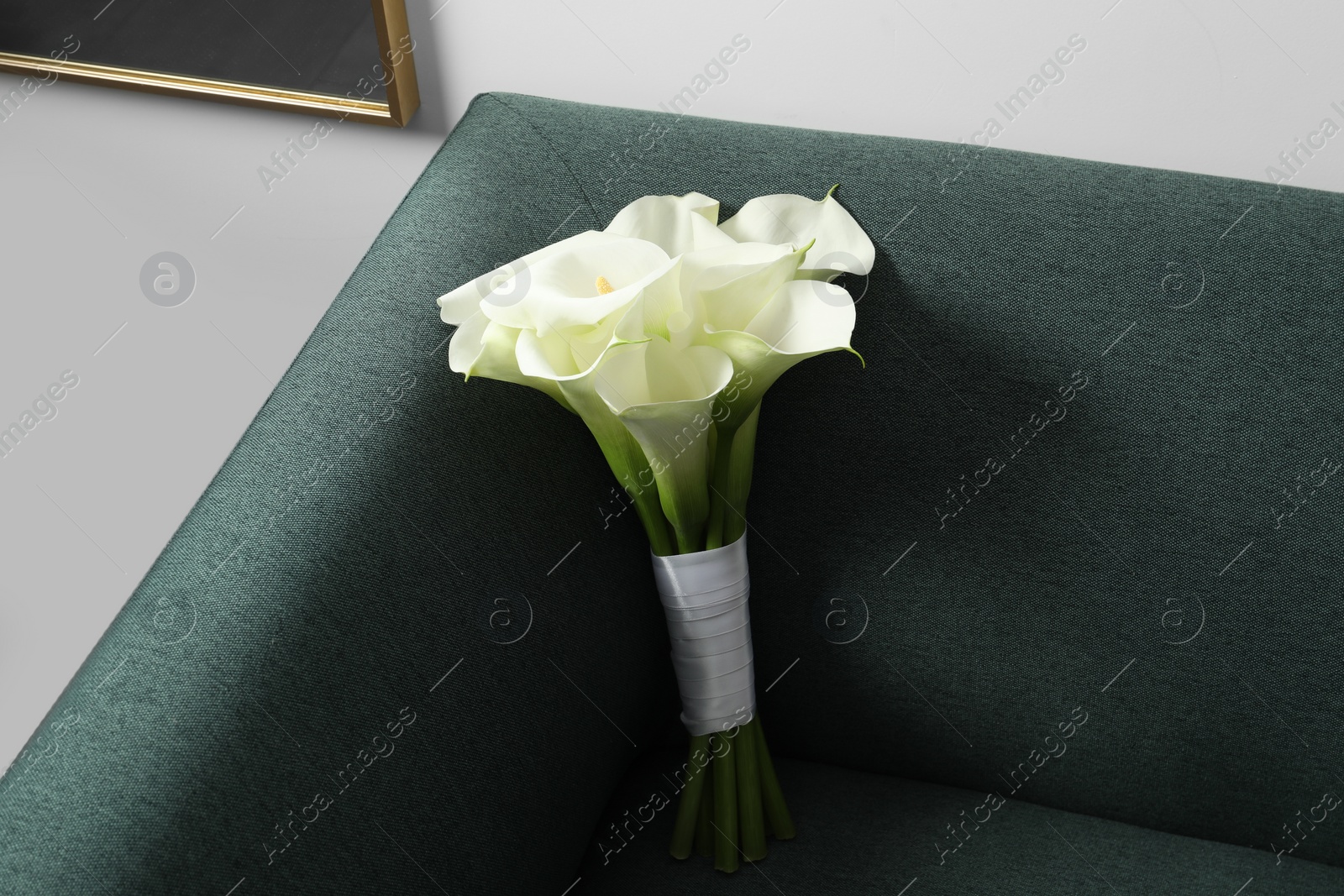 Photo of Beautiful calla lily flowers tied with ribbon on sofa indoors