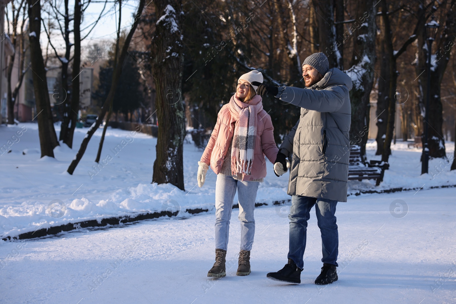 Photo of Happy couple walking in sunny snowy park. Space for text