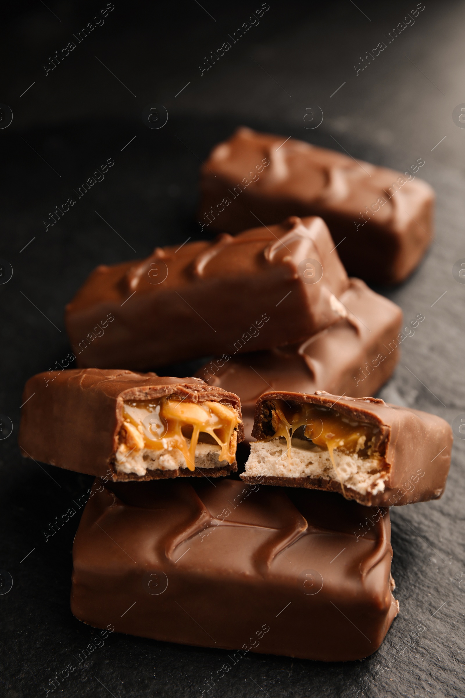 Photo of Chocolate bars with caramel, nuts and nougat on black table, closeup