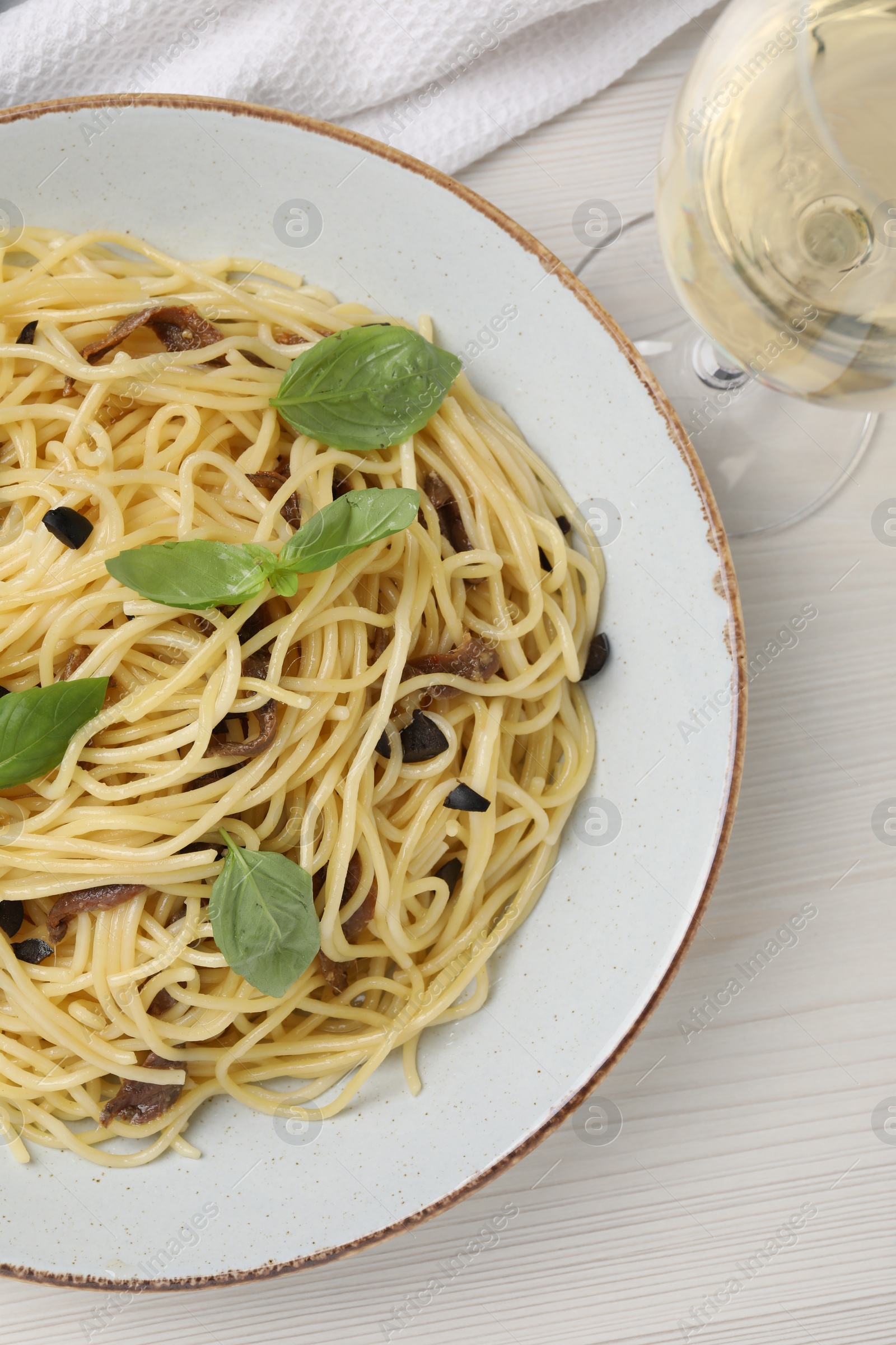 Photo of Delicious pasta with anchovies, olives and basil on white wooden table, top view