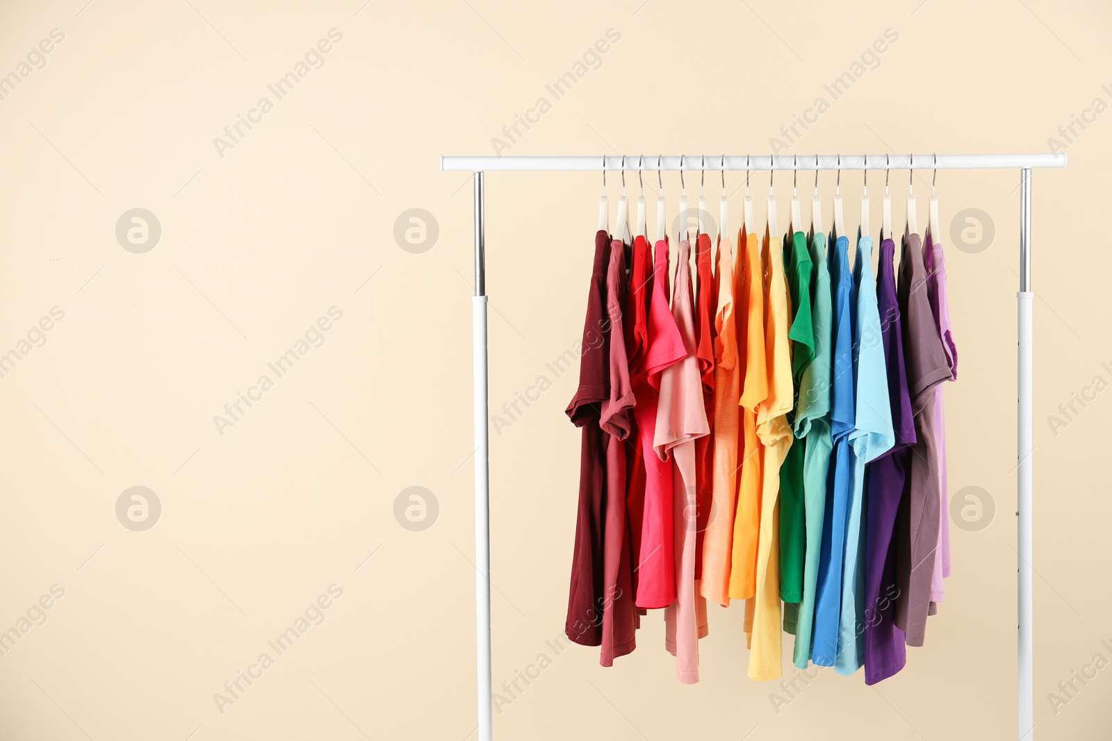 Photo of Many t-shirts hanging in order of rainbow colors on light background