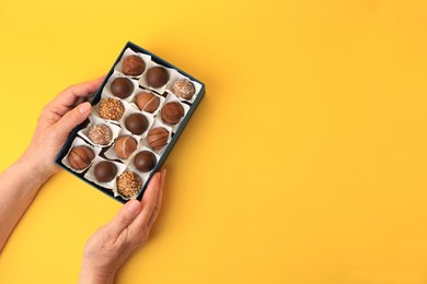 Photo of Woman with box of delicious chocolate candies on yellow background, top view. Space for text