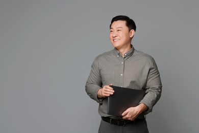 Photo of Portrait of happy businessman with laptop on grey background. Space for text