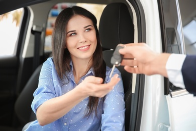 Salesman passing key to young woman in auto at dealership. Buying new car