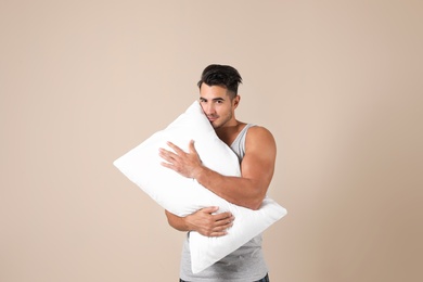 Young man with soft pillow on color background