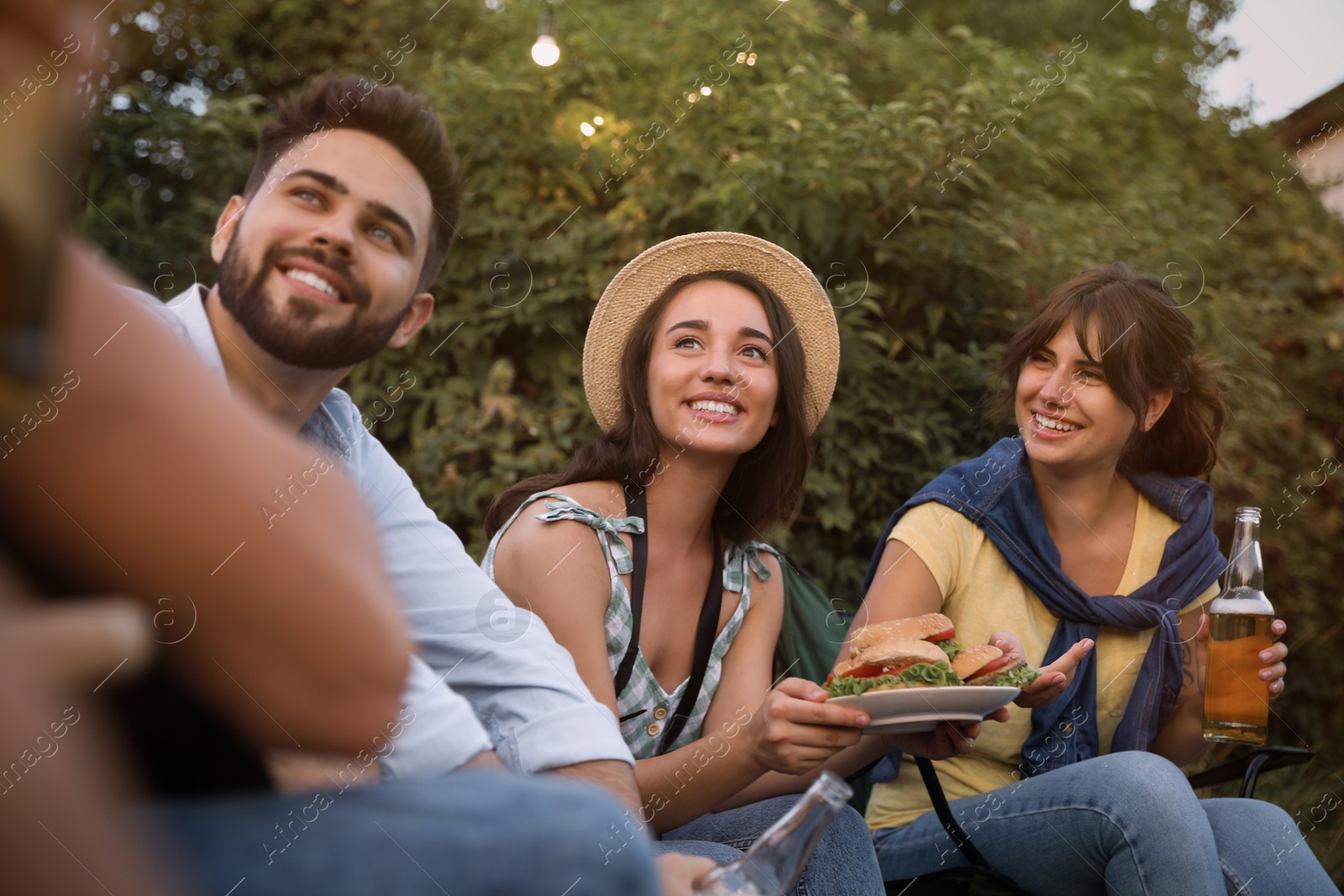 Photo of Happy friends with burgers and beer resting outdoors. Camping season