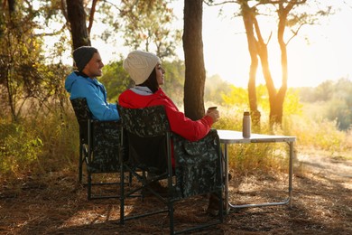 Photo of Couple resting in camping chairs and enjoying hot drink outdoors