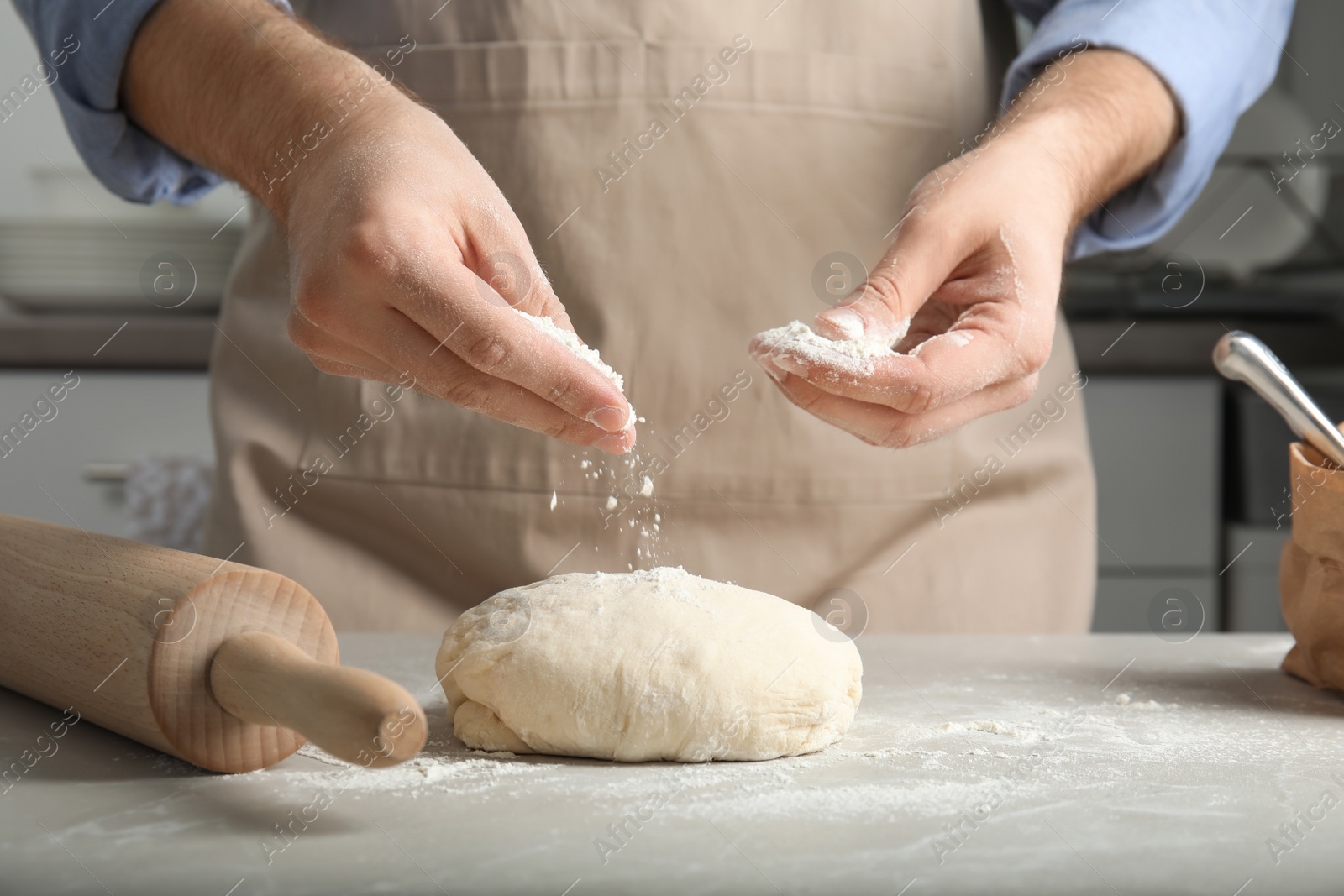 Photo of Man sprinkling dough for pastry with flour on table