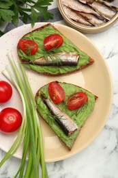 Photo of Delicious sandwiches with sprats, tomatoes, avocado puree and dill on white marble table, flat lay