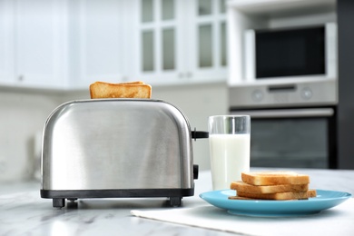Photo of Modern toaster with slices of bread and milk on white marble table in kitchen