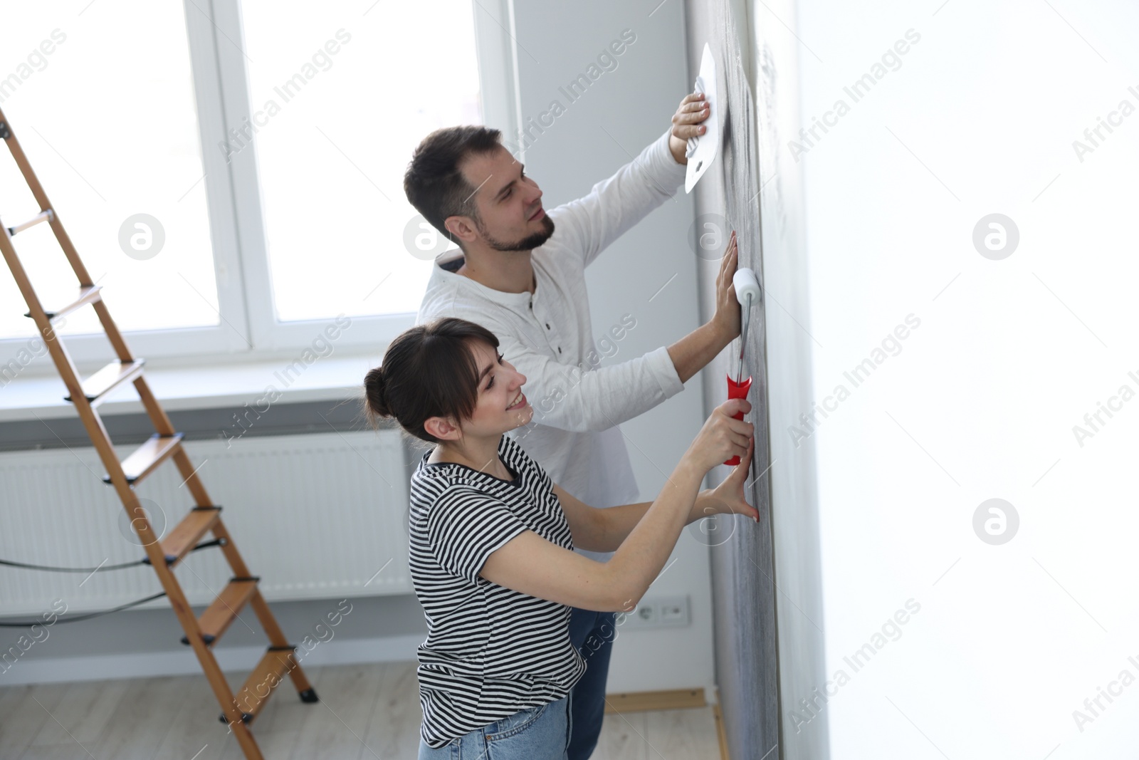 Photo of Woman and man hanging wallpaper in room