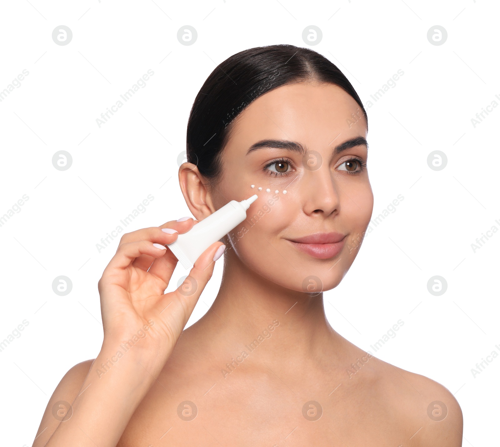 Photo of Beautiful young woman applying cream on skin under eye against white background