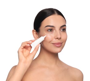 Photo of Beautiful young woman applying cream on skin under eye against white background