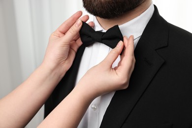 Photo of Woman adjusting bow tie to man indoors, closeup