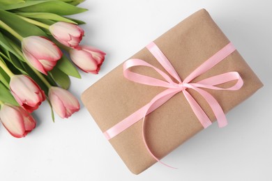 Beautiful gift box with bow and pink tulips on white background, flat lay