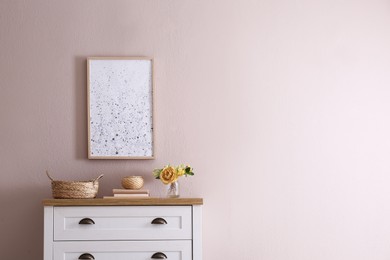 Photo of Beautiful bouquet, books and decor on chest of drawers near beige wall indoors, space for text. Interior design