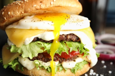 Photo of Closeup view of tasty burger with fried egg on blurred background