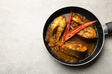 Photo of Tasty fish curry in frying pan on light grey table, above view. Space for text. Indian cuisine