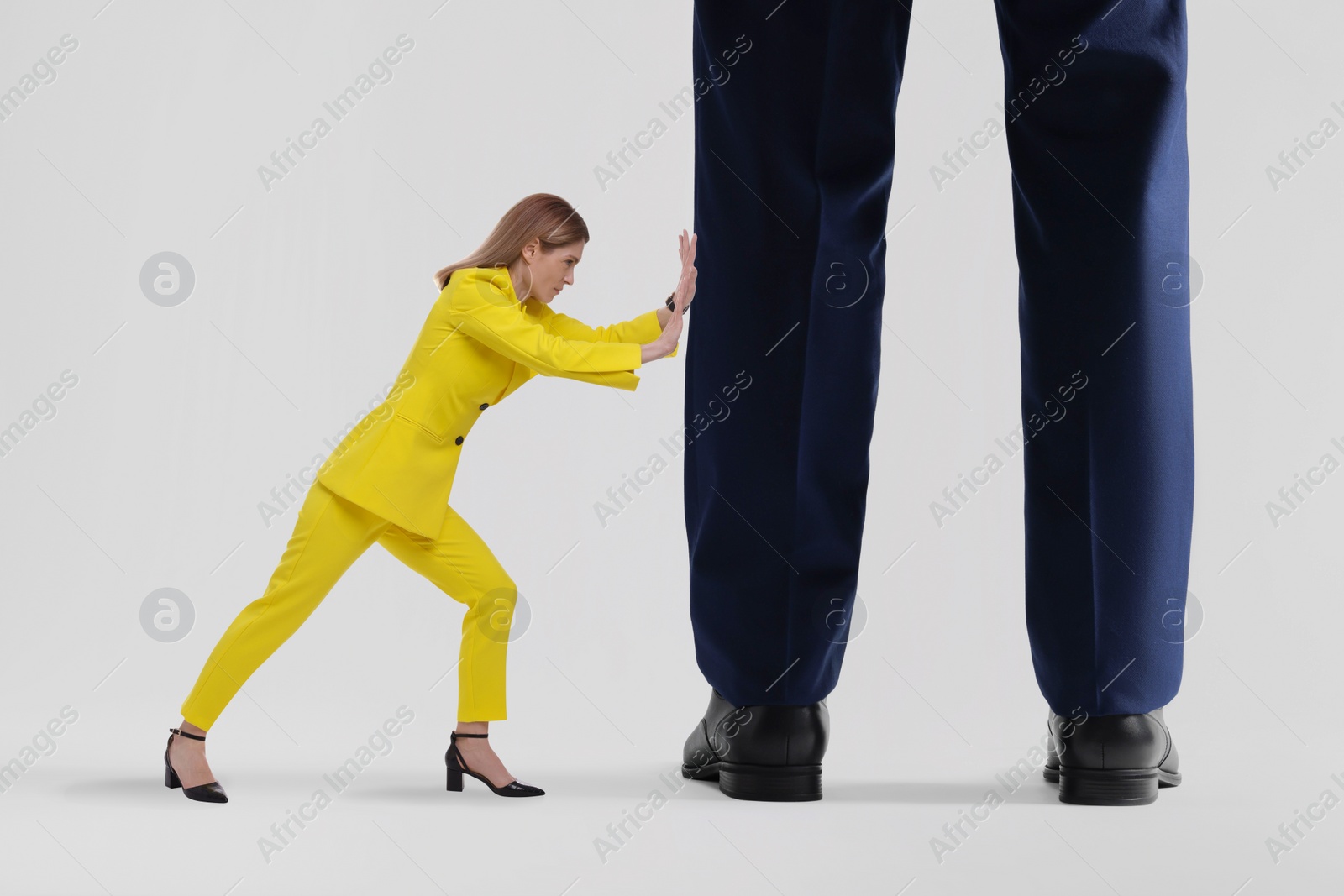 Image of Small woman pushing giant man on light background