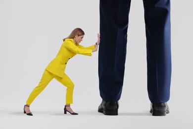 Small woman pushing giant man on light background