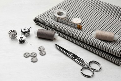 Photo of Composition with different sewing supplies and fabric on white wooden table