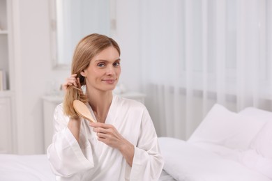 Photo of Beautiful woman brushing her hair on bed in room