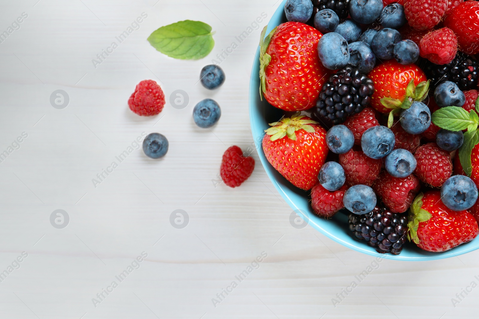 Many different fresh ripe berries in bowl on white wooden table, flat lay. Space for text Photo of Many different fresh ripe berries in bowl on white wooden table, flat lay. Space for text