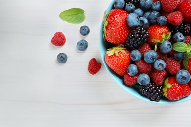 Photo of Many different fresh ripe berries in bowl on white wooden table, flat lay. Space for text