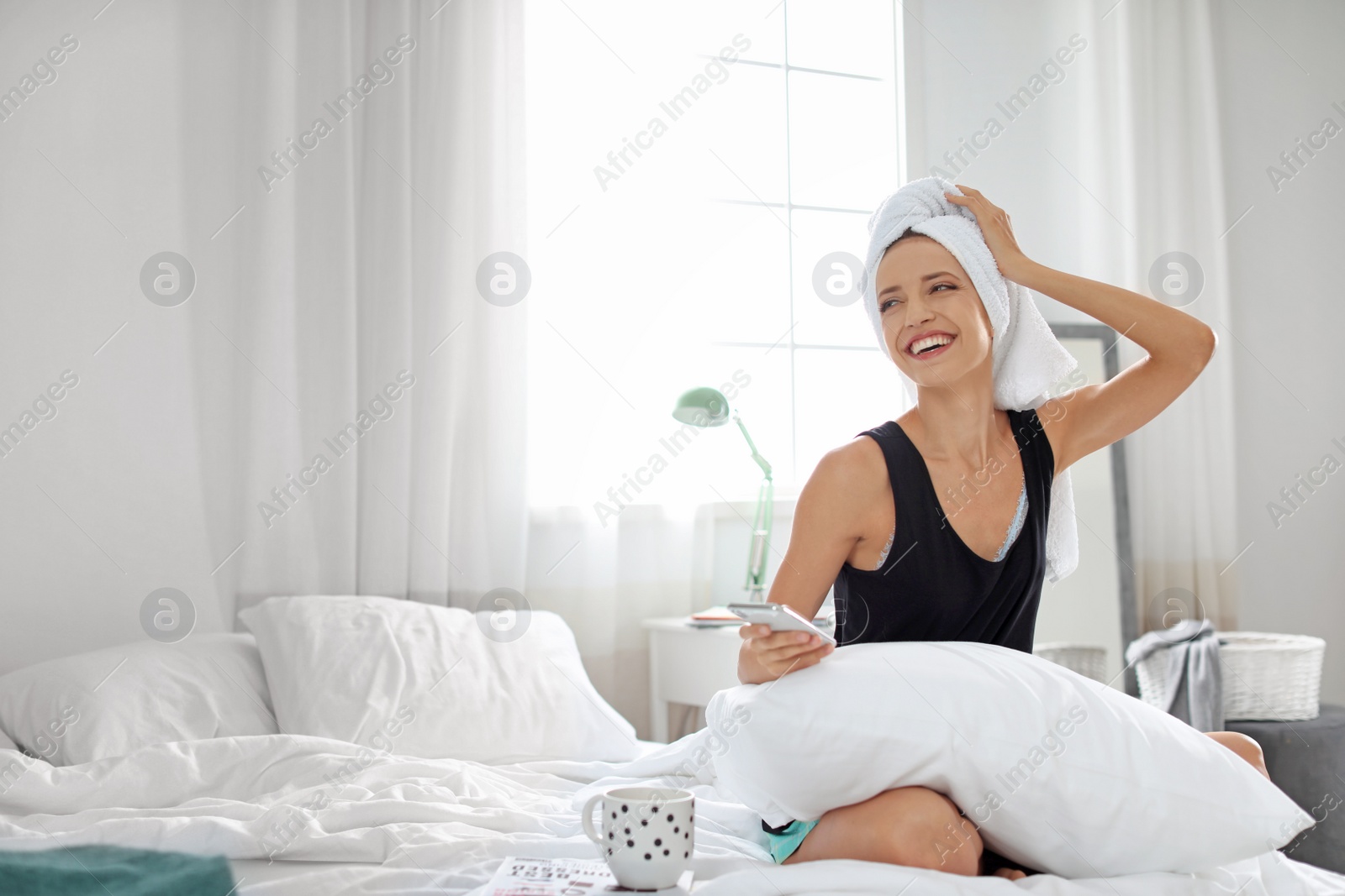 Photo of Young happy woman with mobile phone on bed at home. Lazy morning