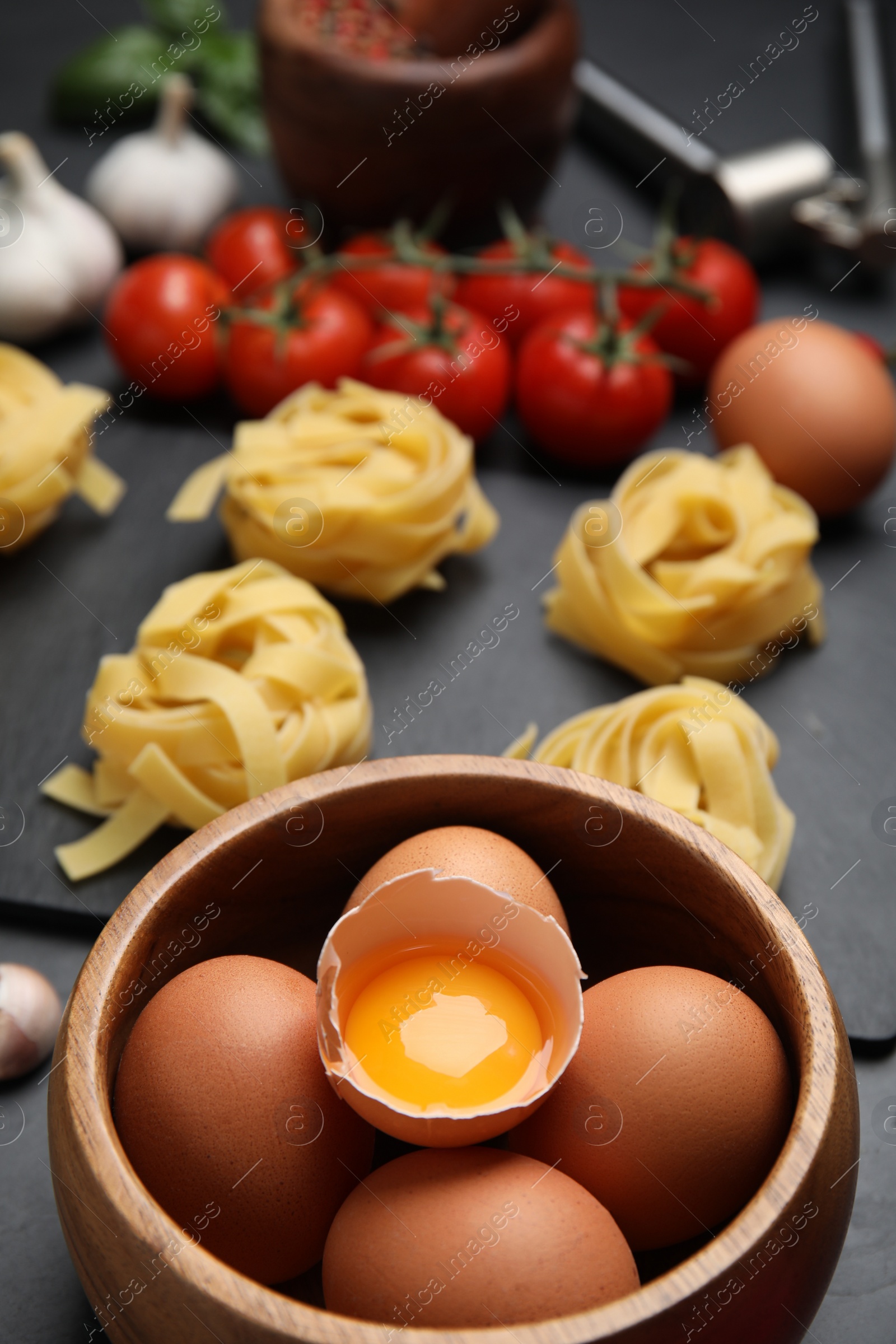 Photo of Raw eggs, uncooked tagliatelle and fresh ingredients on black table, closeup