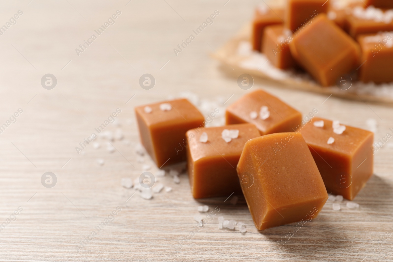 Photo of Tasty caramel candies and sea salt on light wooden table, closeup. Space for text