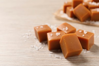 Photo of Tasty caramel candies and sea salt on light wooden table, closeup. Space for text