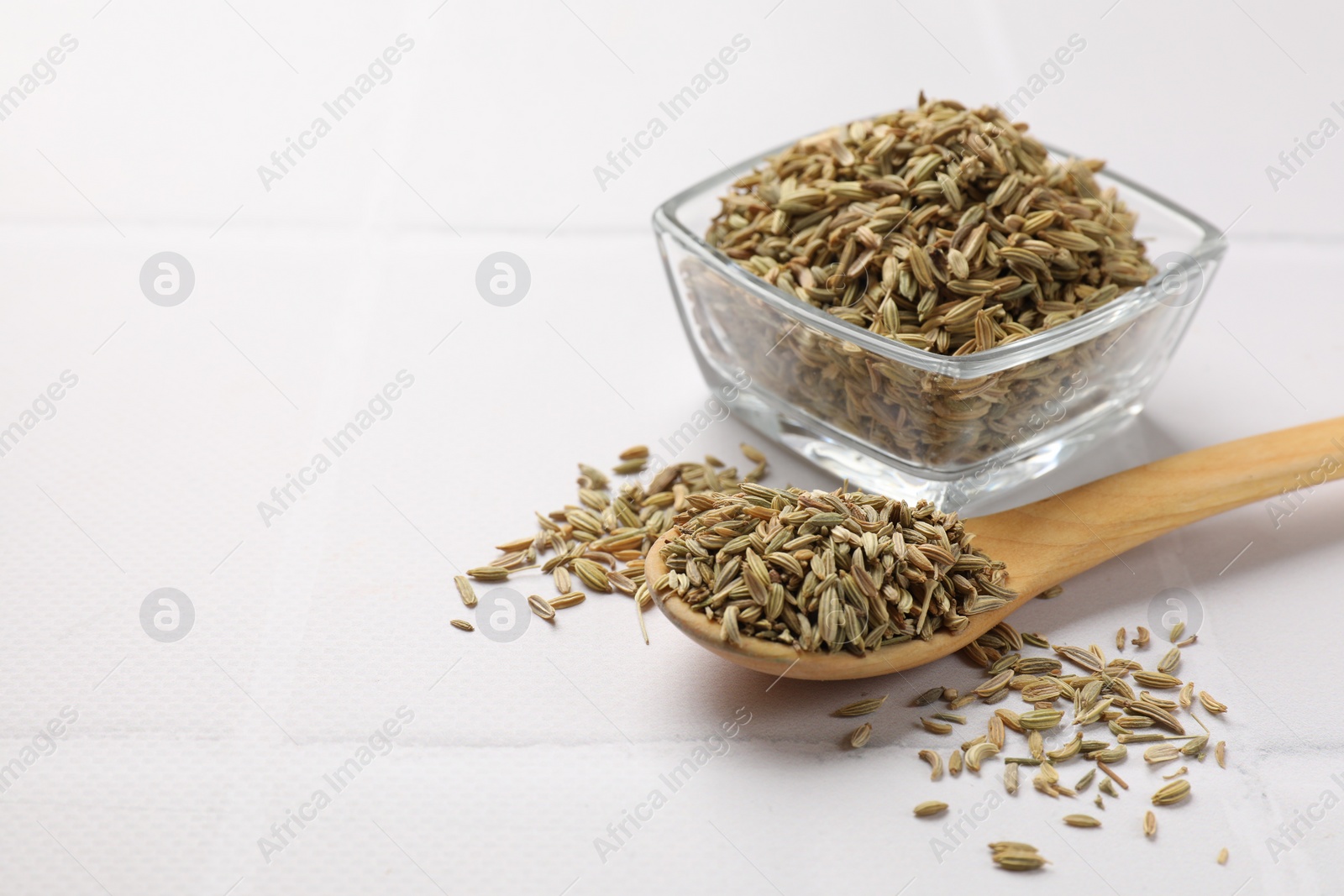 Photo of Bowl and spoon with fennel seeds on white table. Space for text