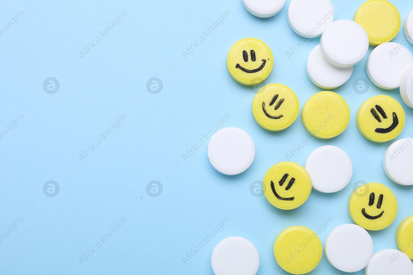 Photo of Many antidepressant pills with happy faces on light blue background, flat lay. Space for text