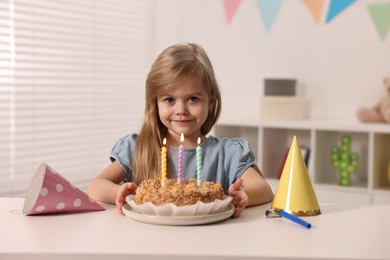 Cute girl with birthday cake at table indoors