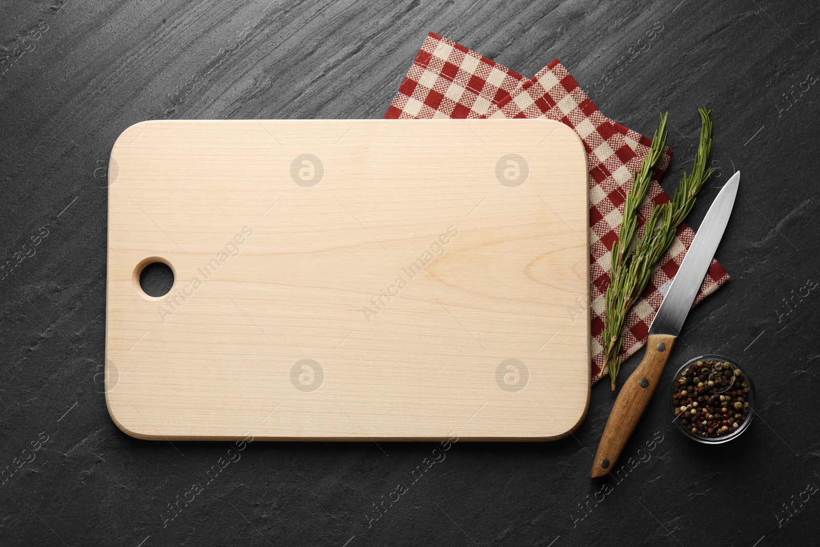 Photo of Wooden cutting board, spices, knife and kitchen towel on dark grey table, flat lay