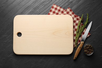 Wooden cutting board, spices, knife and kitchen towel on dark grey table, flat lay