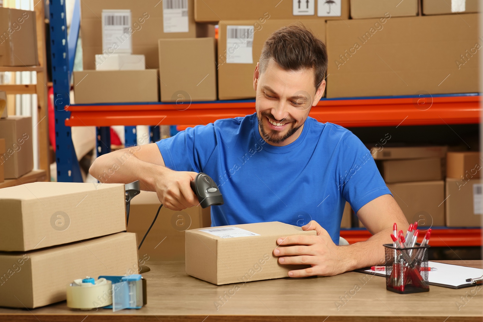 Photo of Post office worker with scanner reading parcel barcode at counter indoors