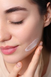 Photo of Young woman with dry skin applying cream onto her face, closeup