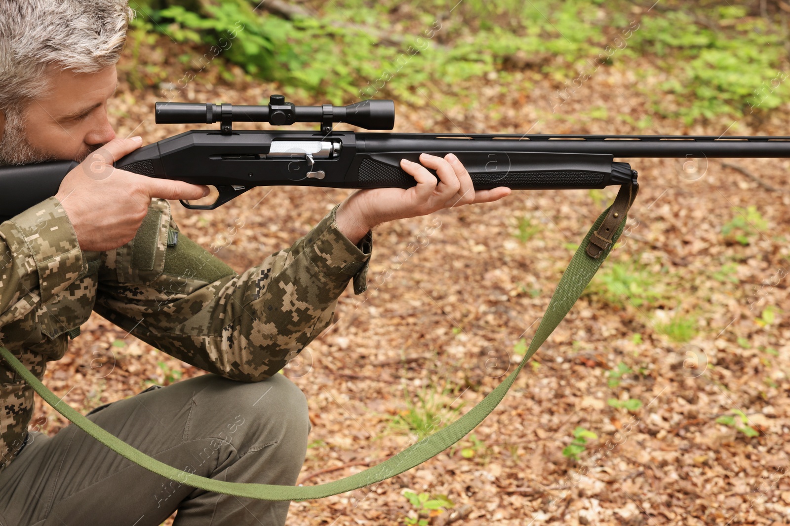 Photo of Man wearing camouflage and aiming with hunting rifle in forest, closeup