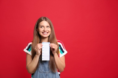 Photo of Portrait of happy young woman with lottery ticket on red background, space for text