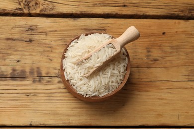 Photo of Raw basmati rice in bowl and scoop on wooden table, top view